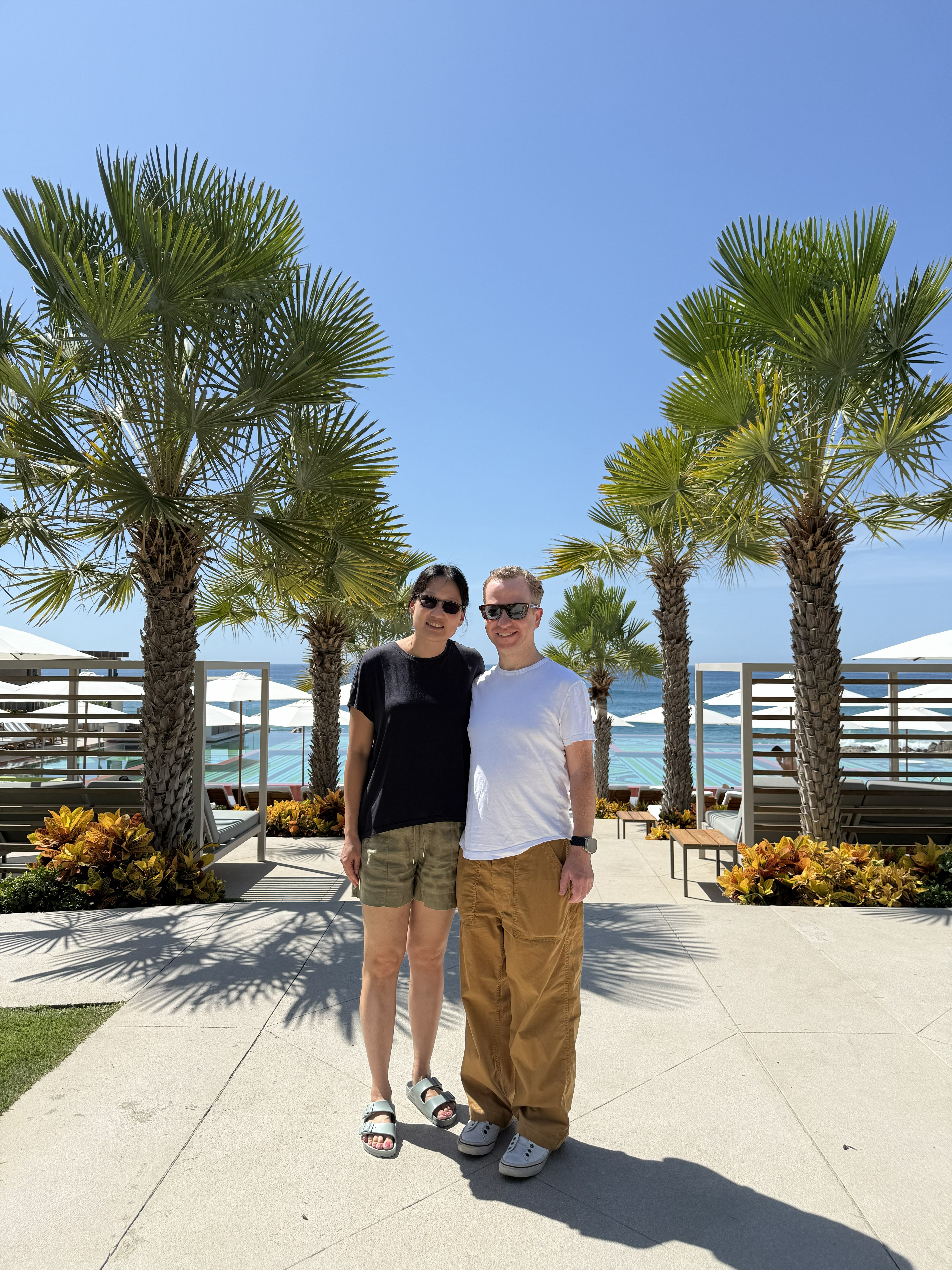 DrEgalkaandhiswifestandinfrontofpalmtreesandtheocean