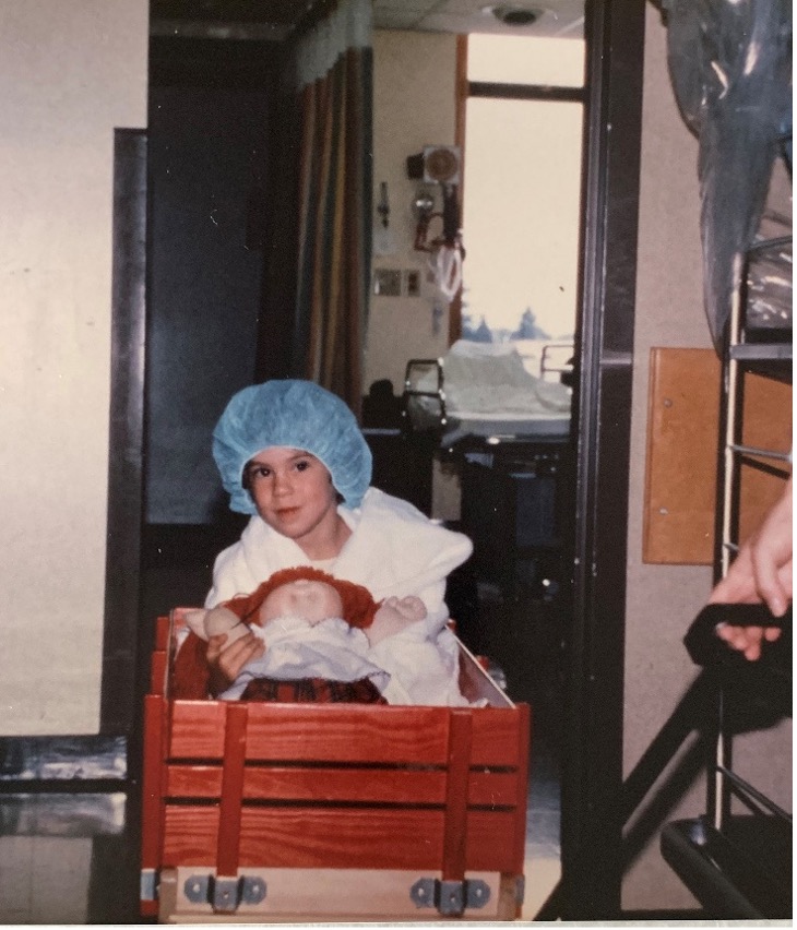 Sarah Horn as a child holds a Cabbage Patch doll in a red wagon being pulled.