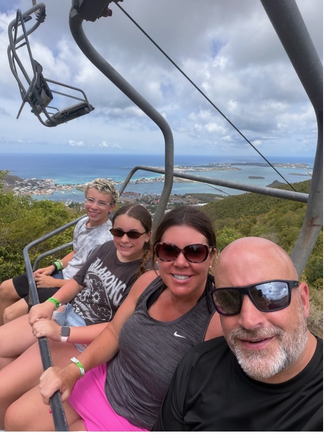 Sarah Horn with her husband and two children on a ski lift with green hills and water behind.