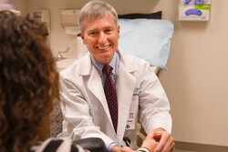 DoctorinwhitelabcoatisfacingapatientwhilesmilingandcheckingtheirhandsPatientisfacingthedoctor