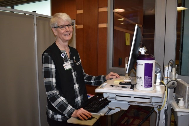 Lani Women is standing next to a computer monitor smiling at the camera.