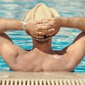 Maninsunhatrelaxingonsideofswimmingpoolonsummervacation