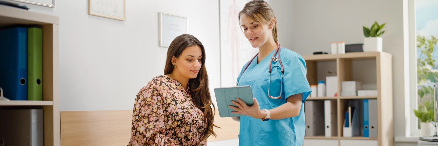 ALatinawomaninacolorfuldresshasamedicalexamwithanursewearingbluescrubs