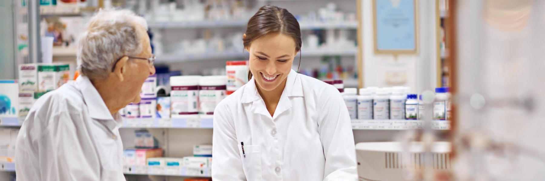 Ayoungwomanpharmacistinawhitecoatassistsandelderlymanattheretailcounter