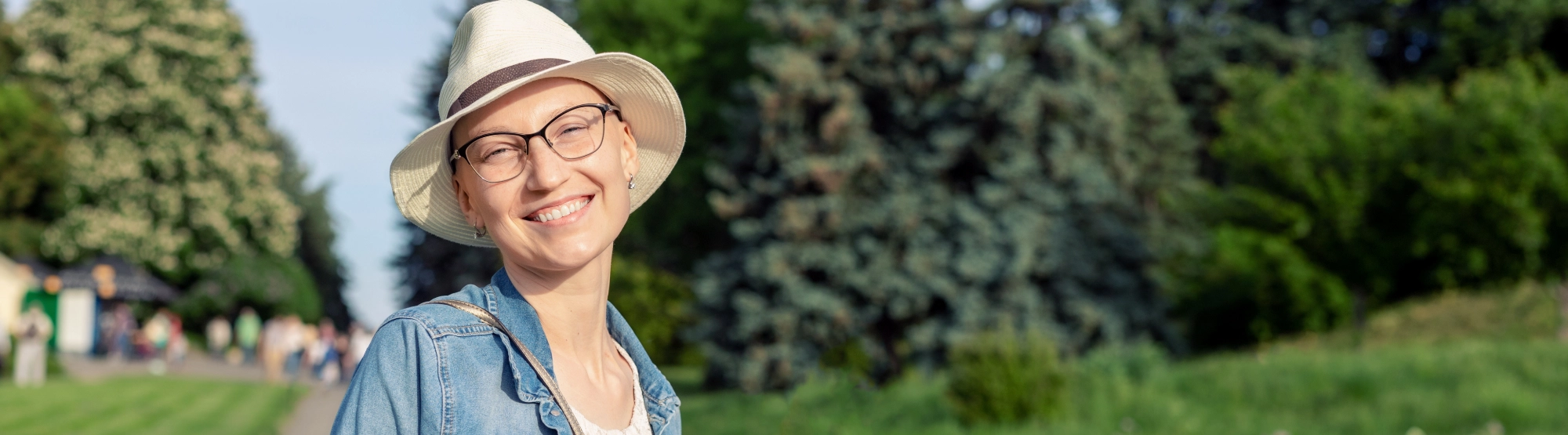 Ahappywomanwearingahatandstandingonaparkpath