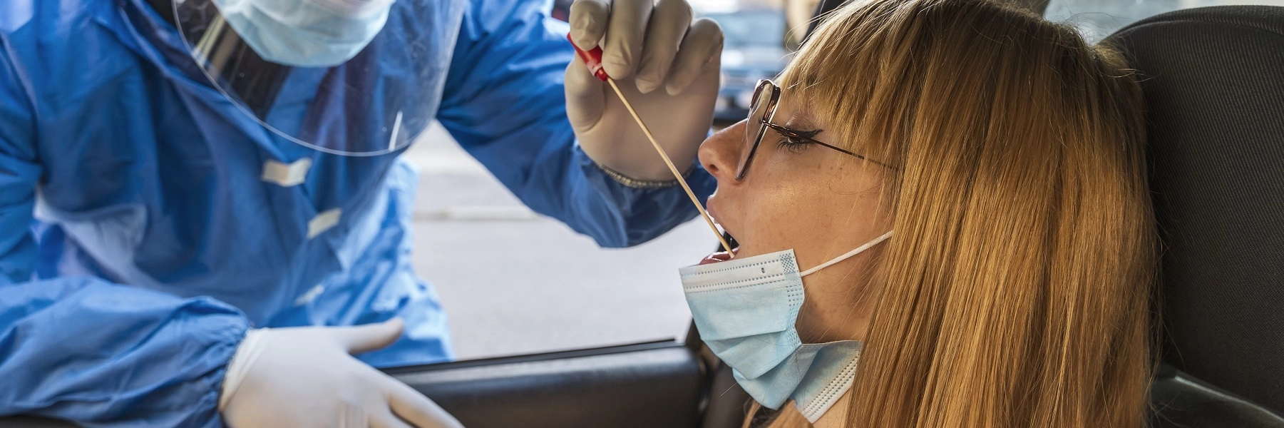 Awomaninacarspassengerseathashermouthswabbedbyamalelabworkerinfullprotectiveequipment