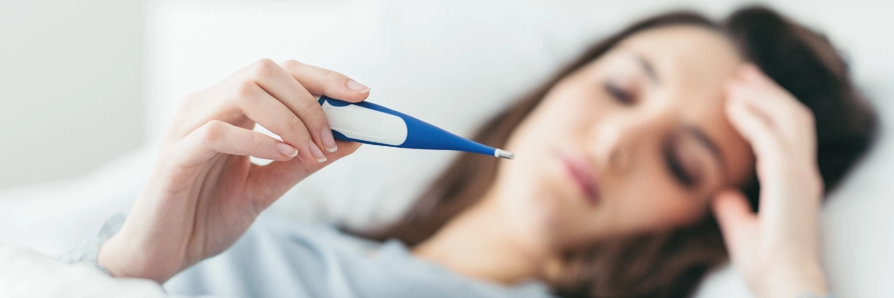 Awomaninbedlooksatathermometer