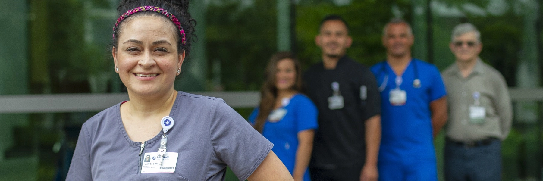 AHispanicwomaningrayscrubsstandsinfrontofagroupofSalemHealthemployees