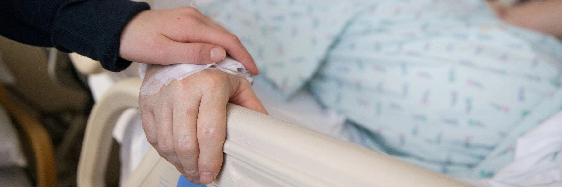 Avisitorholdsthehandofanelderlypatientinahospitalbed