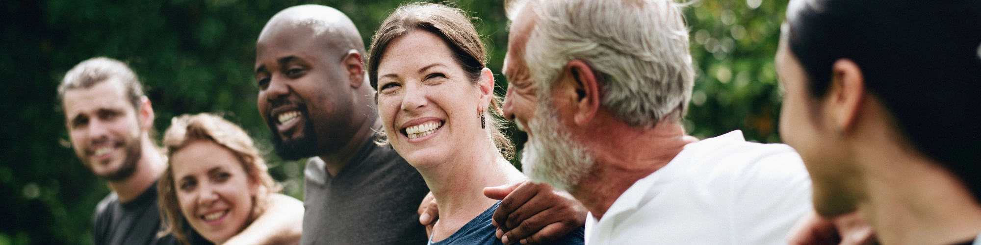 Groupofdiversepeoplestandingoutsidewiththeirarmsovereachothersshoulders