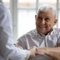 Ahappyelderlymansittingandholdinghandswithhisdoctor
