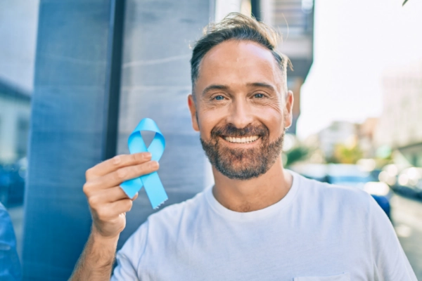 Man standing outside holding a blue prostate cancer ribbon.