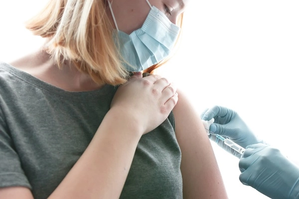 Awomanwearingamaskreceivesavaccinationfromamedicalprofessional