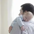Afatherholdinghisnewsleepybabyoverhisshoulder