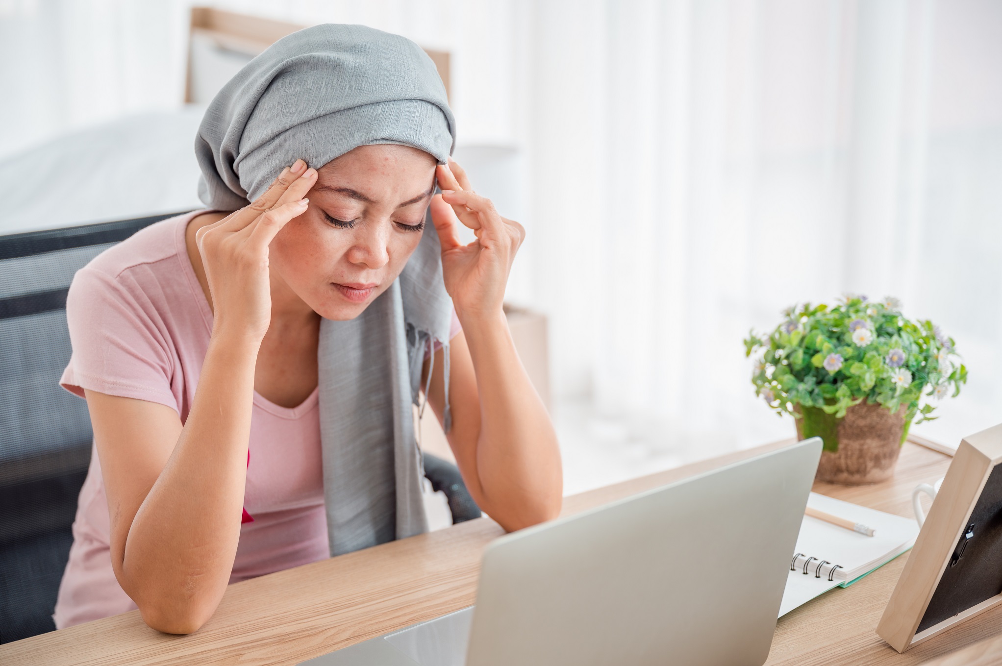 Womaninaheadscarfsitswithhertemplehandatherlaptop