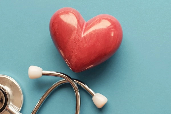 A red polished stone in the shape of a heart lays next to a stethoscope.