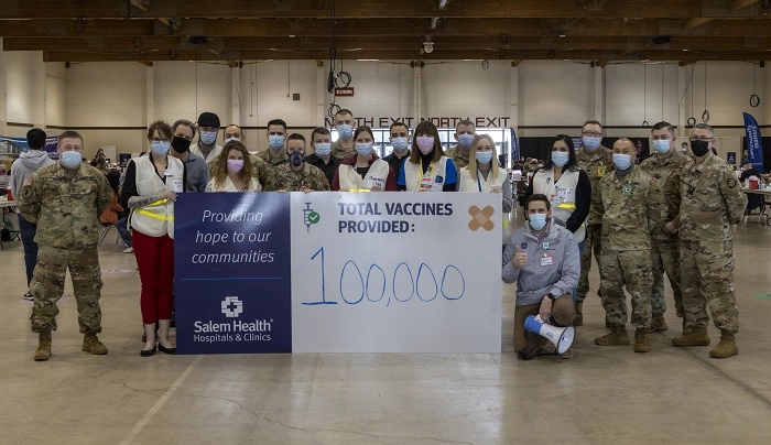 A group of Salem Health staff and national Guard at the State Fairgrounds Vaccine Clinic with the sign reading 100,000.