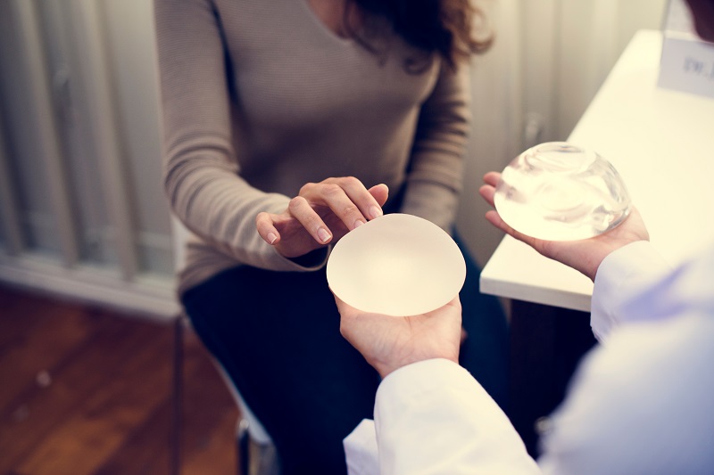 Plastic surgeon showing woman different kinds of breast implants