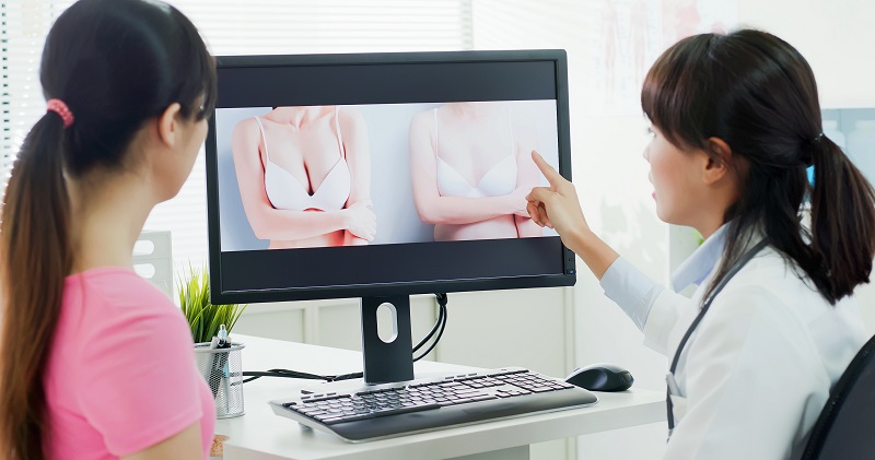 Plastic surgeon and patient looking at breast surgery options on computer