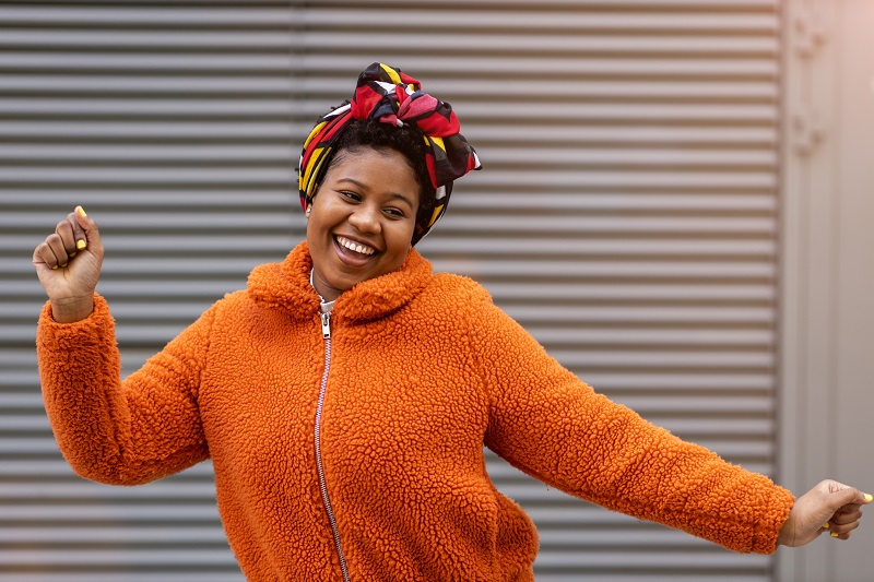 Happy young woman dancing in front of a wall