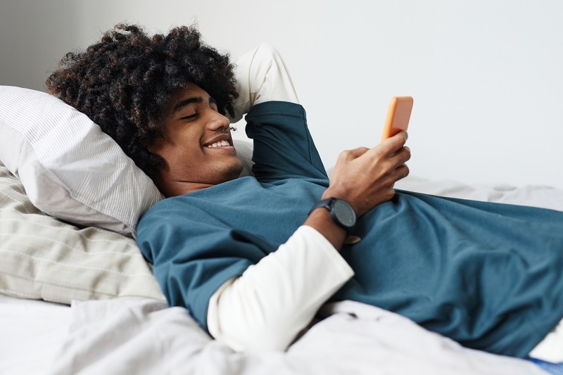 Male college student using smartphone in his dorm