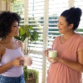 motherandadultdaughterholdingcupstalkingathome