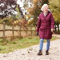ActiveSeniorWomanOnAutumnWalkWithDogOnPathThroughCountryside