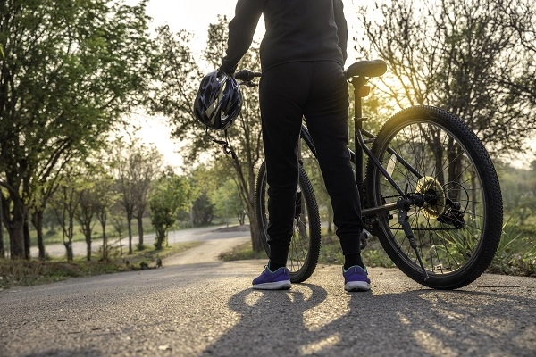 A woman stands beside a bicycle holding a helmet.