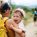 Rearviewofmotherwithsmallcryingdaughterhikingoutdoorsinsummernature