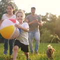 Childrendadanddogrunintheparkplayingwithabeachball