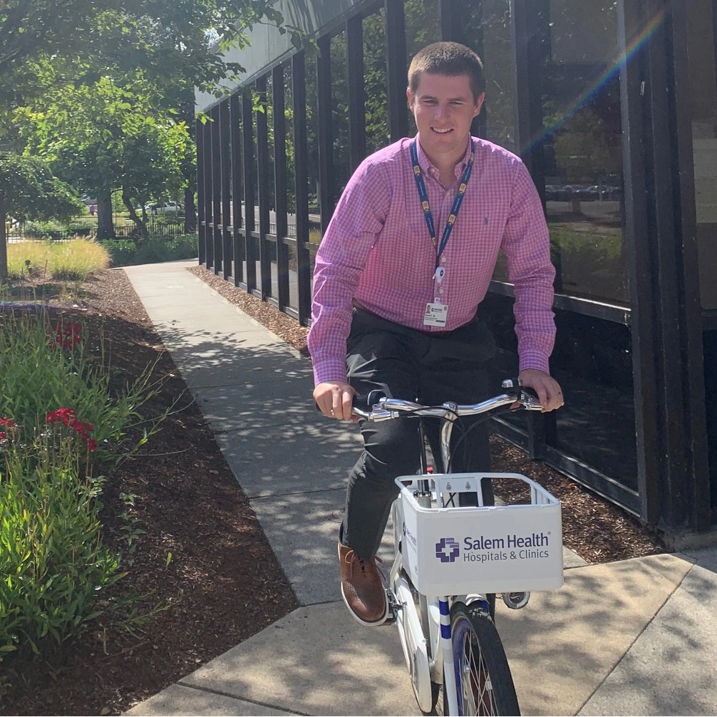 Bryce Peterson, Salem Health director of community outreach on a bike share bike in front of Building B.