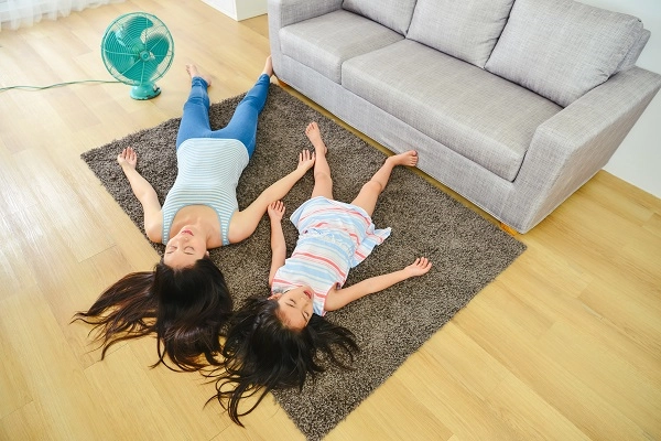 A woman and a little girl sleep on a rug in front of an electric fan.