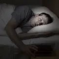 Photoillustrationofawhitemanlayingawakeinbed