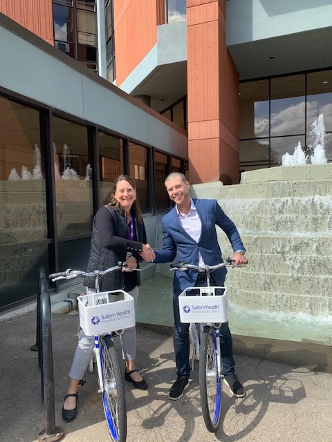 Vice President for Community Engagement Leilani Slama, pictured with Ride Salem organizer Evan Osborne on bike share bikes in front of Building B.