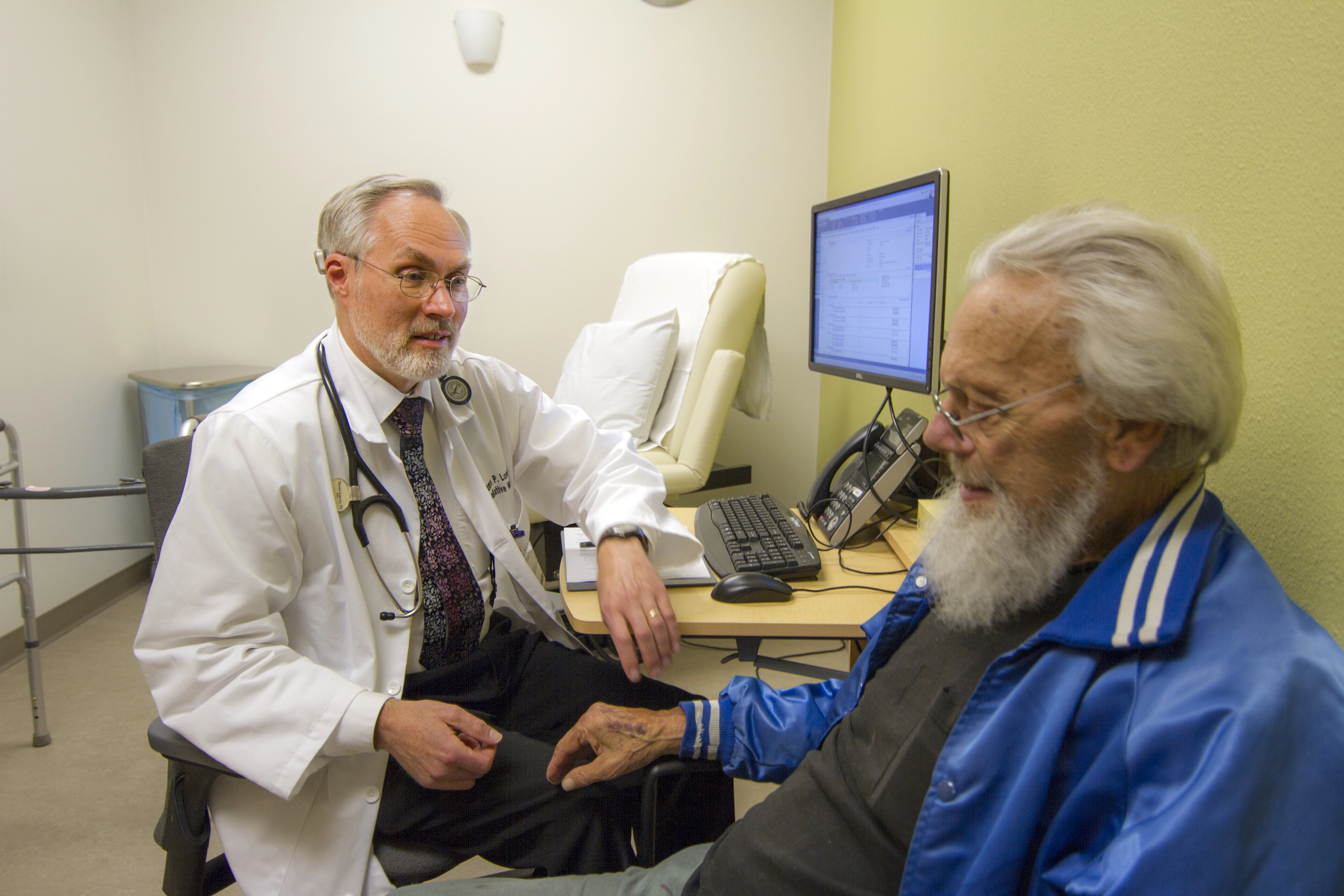 Adoctorsittingathisdeskspeakingtoapatientinabluejacket