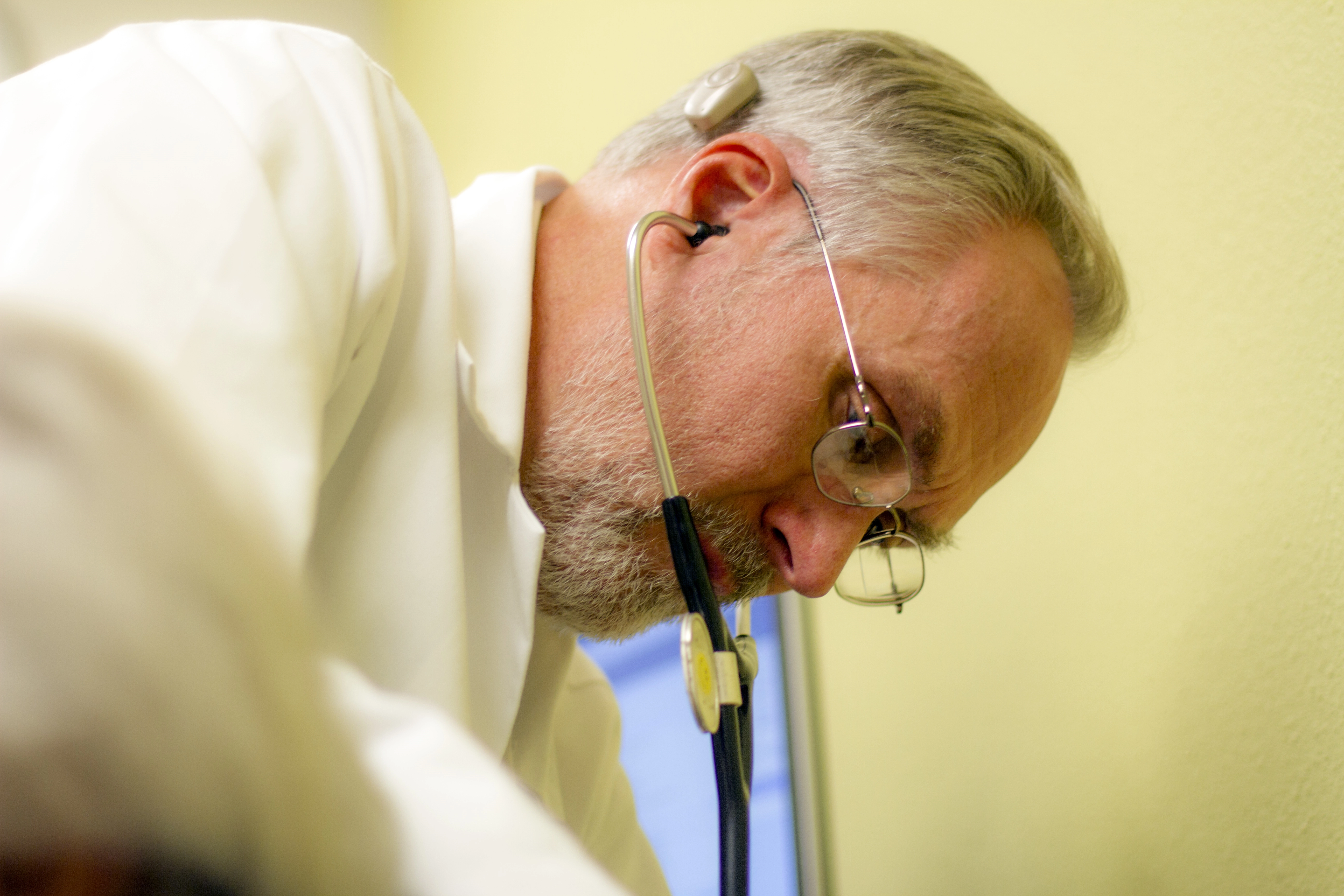 Adoctorwithstethoscopeinhisearspeeringdownwards