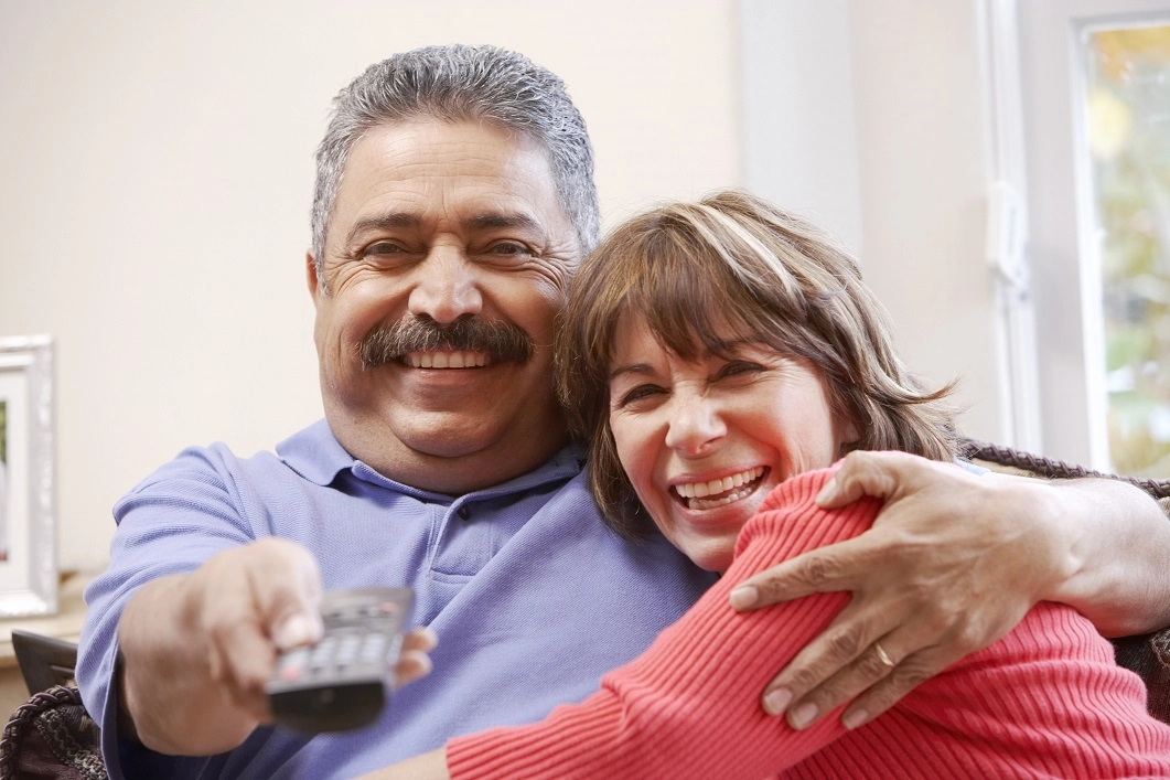 Amanandawomaninsmilingembracewhilethemanusesaremotecontrolclicker