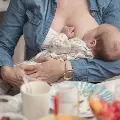 Womanwearingajeanjacketbreastfeedsaninfantatatablesetforlunch