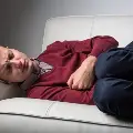 Manlayingonacouchclutchinghisstomachandfrowning