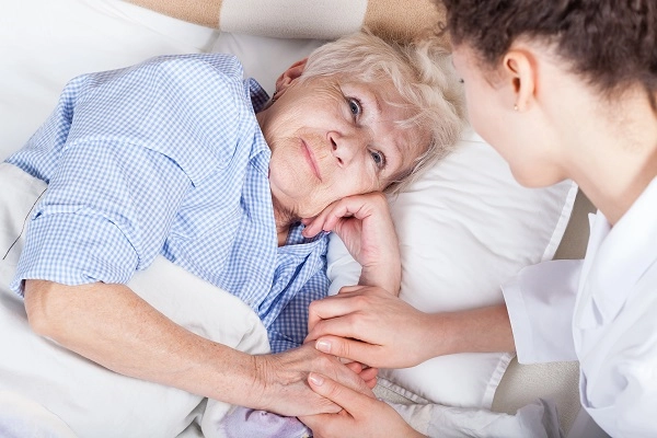 Elderly woman looks up at nurse from her hospital bed.