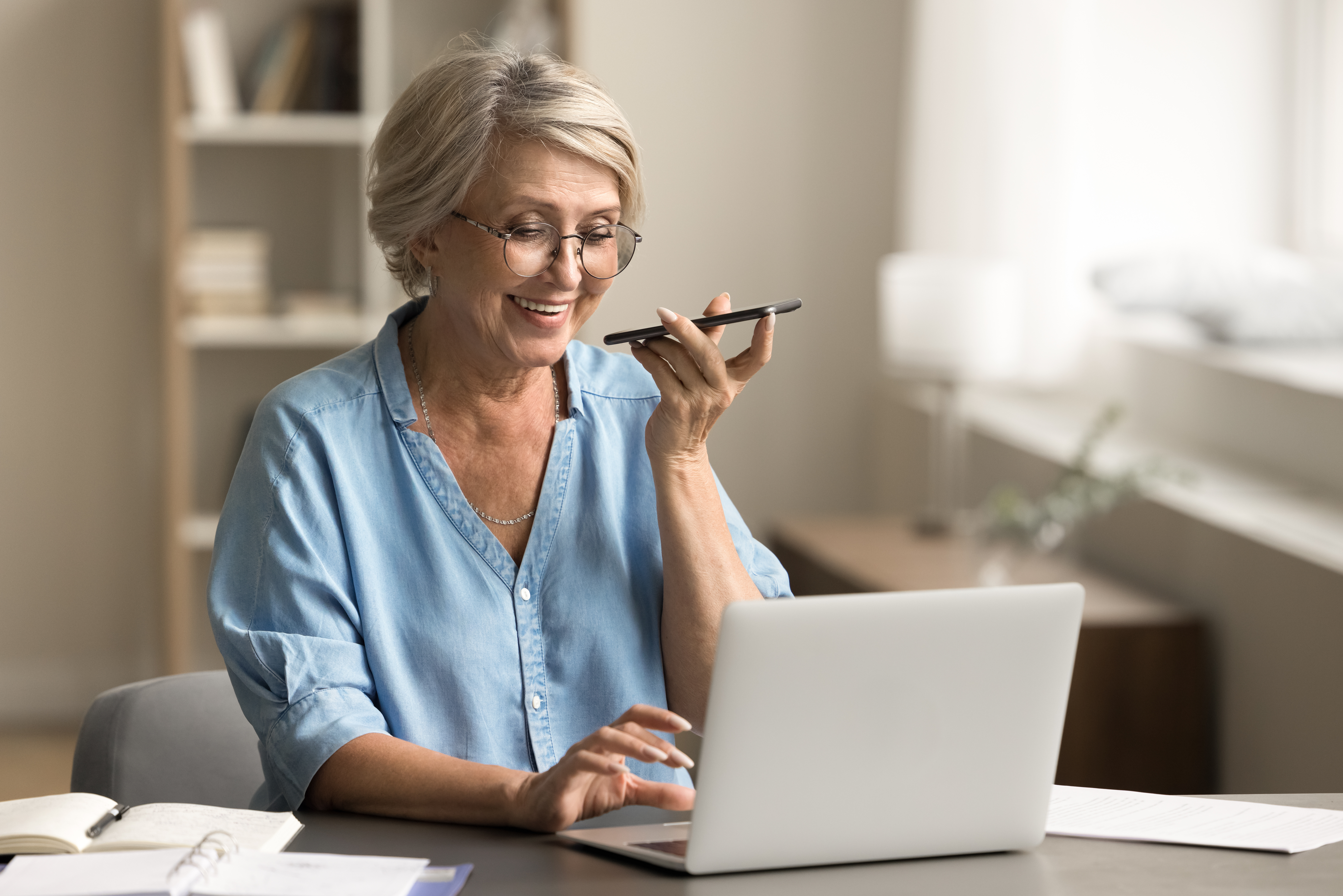 Olderwomanspeaksonacellphonewhilelookingatherlaptop