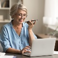 Olderwomanspeaksonacellphonewhilelookingatherlaptop